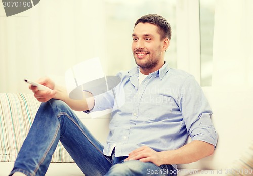 Image of smiling man with tv remote control at home