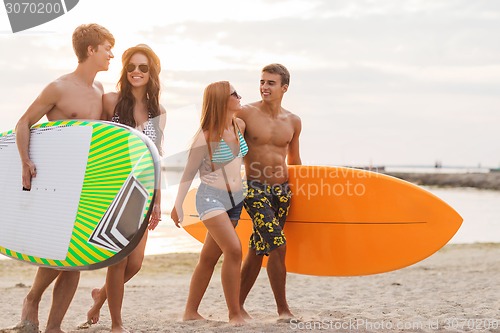 Image of smiling friends in sunglasses with surfs on beach