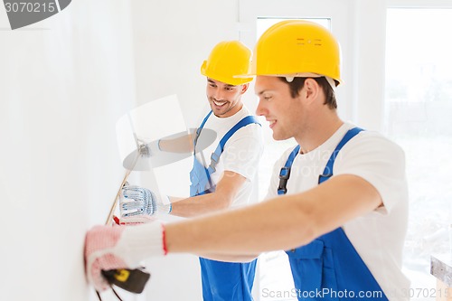 Image of smiling builders with measuring tape indoors