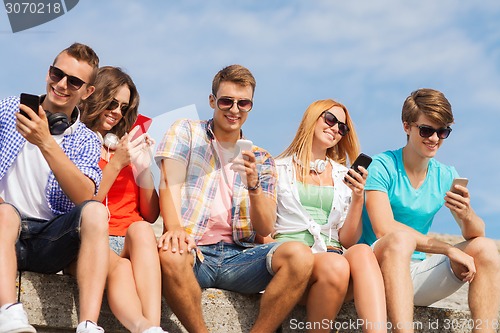 Image of group of smiling friends with smartphones outdoors