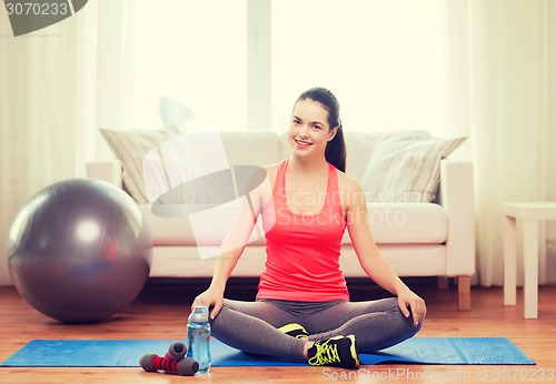 Image of smiling girl sitting on mat with sports equipment