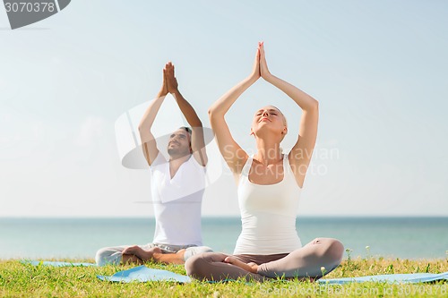 Image of smiling couple making yoga exercises outdoors