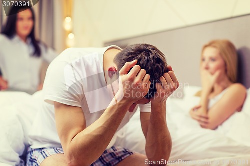 Image of man sitting on the bed with two women on the back