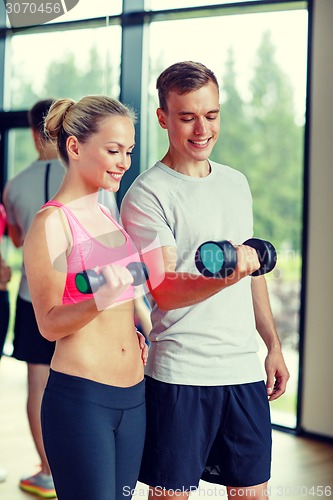 Image of smiling young woman with personal trainer in gym