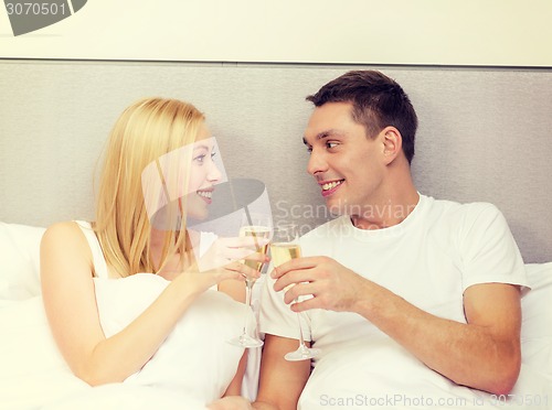 Image of smiling couple with champagne glasses in bed