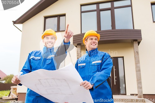 Image of smiling builders with blueprint pointing finger