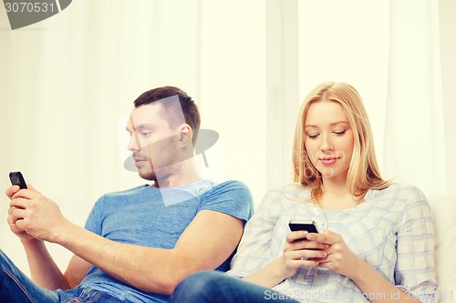 Image of concentrated couple with smartphones at home