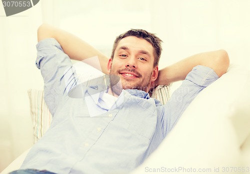 Image of smiling man lying on sofa at home