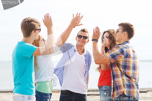 Image of group of smiling friends making high five outdoors