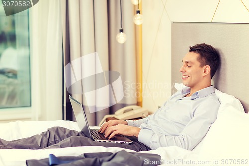 Image of happy businesswoman with laptop in hotel room