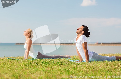 Image of smiling couple making yoga exercises outdoors