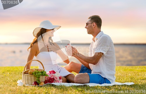 Image of smiling couple with small red gift box on picnic