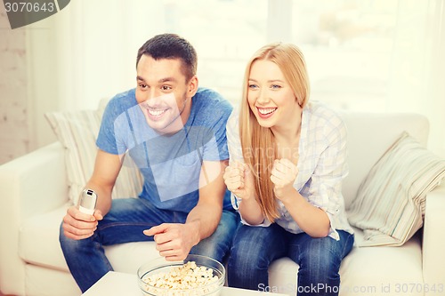 Image of smiling couple with popcorn cheering sports team