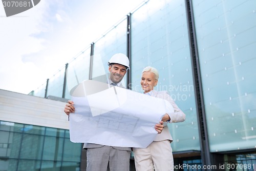 Image of smiling businessmen with blueprint and helmets