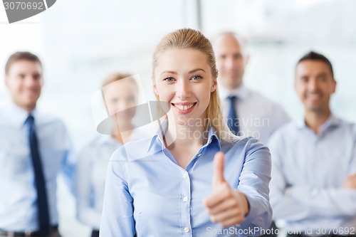 Image of smiling businesswoman showing thumbs up in office