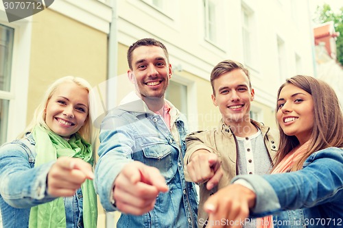 Image of group of smiling friends in city pointing finger