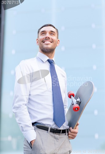 Image of young smiling businessman with skateboard outdoors