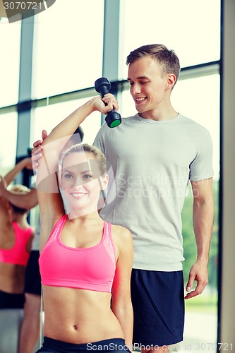 Image of smiling young woman with personal trainer in gym