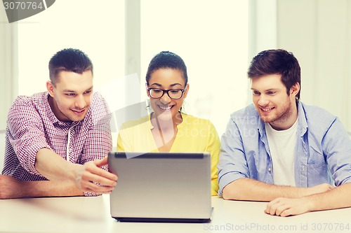 Image of three smiling colleagues with laptop in office