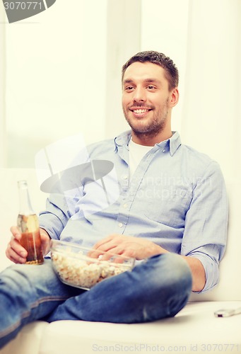 Image of smiling man with beer and popcorn at home