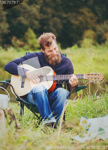 Image of smiling man with guitar and dixie in camping