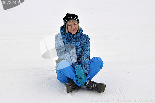 Image of The woman in winter clothes sits on snow.