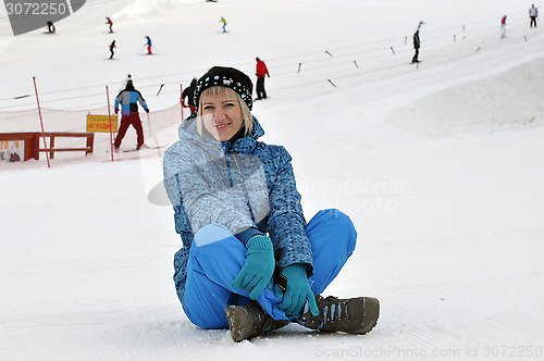 Image of The woman in winter clothes sits on snow against the ski slope a
