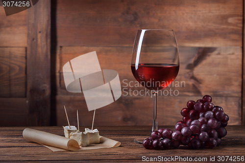 Image of Red wine in glass with grape and cheese on wood