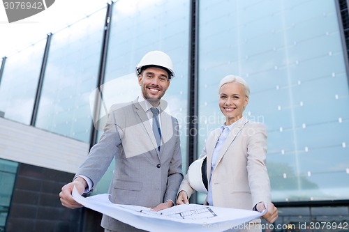 Image of smiling businessmen with blueprint and helmets