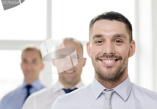 Image of smiling businessman in office with team on back