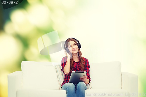 Image of girl sitting on sofa with headphones and tablet pc