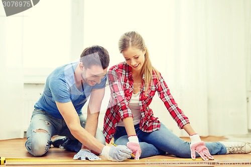 Image of smiling couple measuring wood flooring