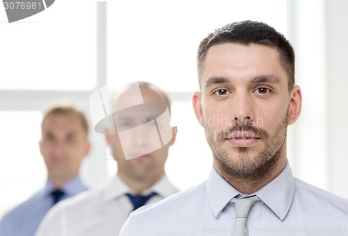 Image of serious businessman in office with team on back