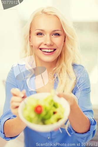 Image of smiling young woman with green salad at home