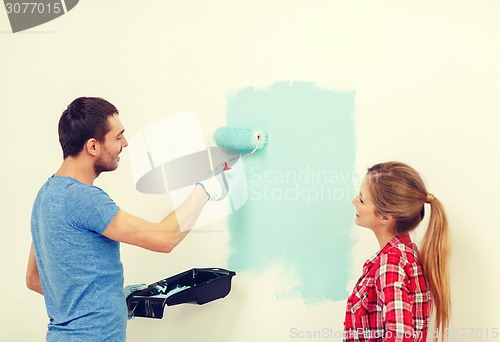 Image of smiling couple painting wall at home