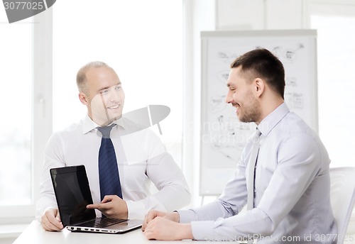 Image of two smiling businessmen with laptop in office