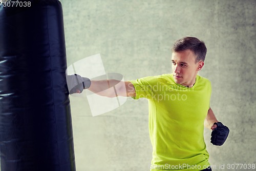 Image of young man in gloves boxing with punching bag