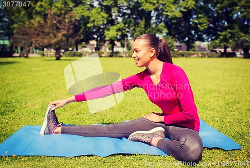Image of smiling woman stretching leg on mat outdoors