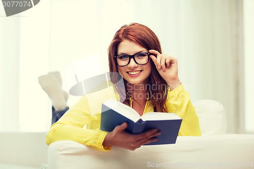 Image of smiling teenager reading book and sitting on couch