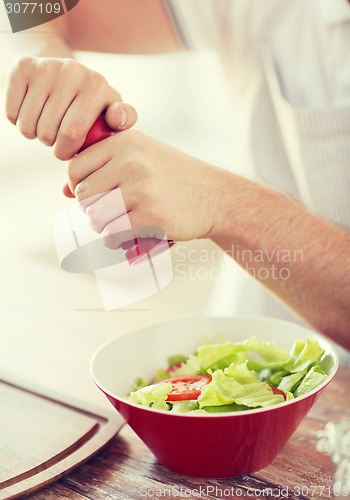 Image of close up of male hands flavouring salad in a bowl