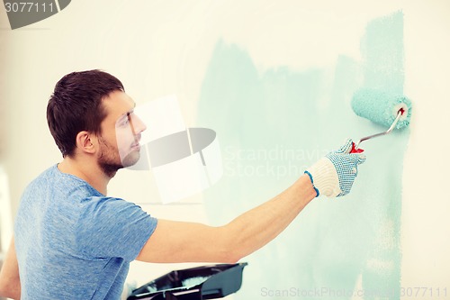 Image of smiling man painting wall at home