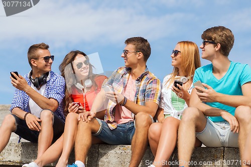 Image of group of smiling friends with smartphones outdoors