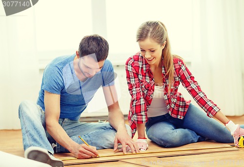 Image of smiling couple measuring wood flooring