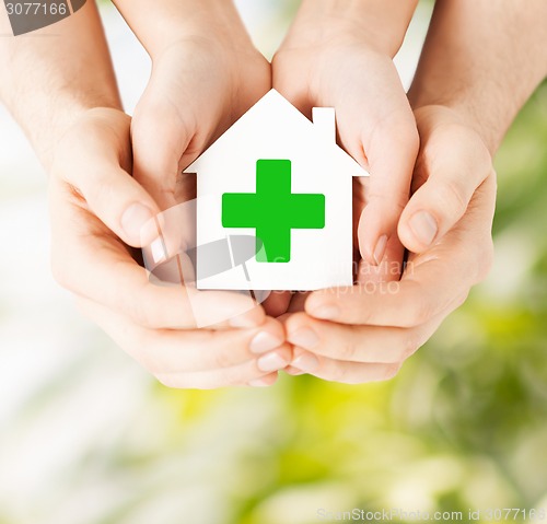 Image of hands holding paper house with green cross