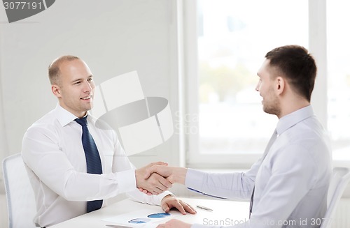 Image of two smiling businessmen shaking hands in office