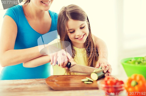 Image of smiling little girl with mother chopping cucumber