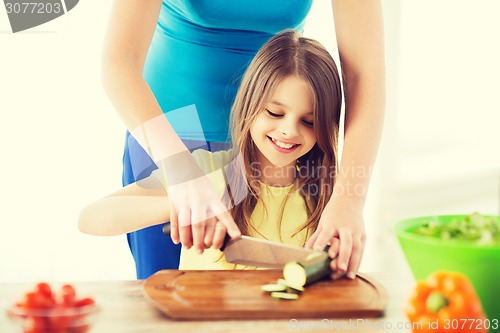 Image of smiling little girl with mother chopping cucumber