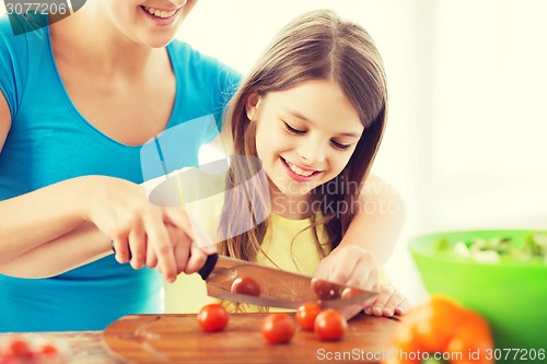 Image of smiling little girl with mother chopping tomatoes