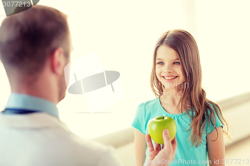 Image of male doctor giving an apple to smiling little girl