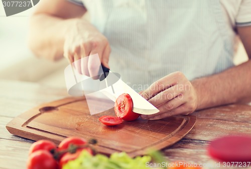 Image of male hand cutting tomato on board with knife